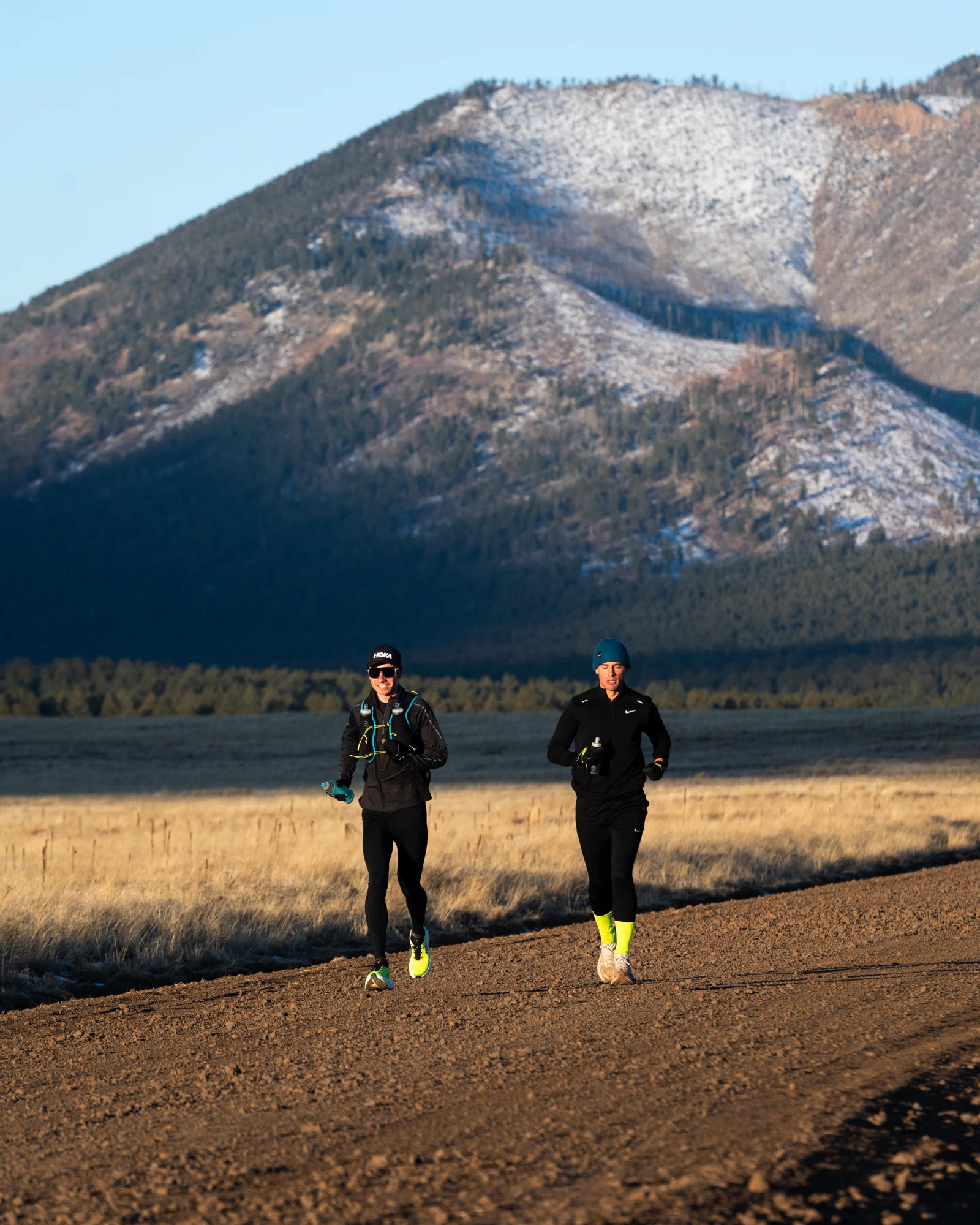 Two Ponderosa Pirates runners cross a meadow with a mountain rising behind them.
