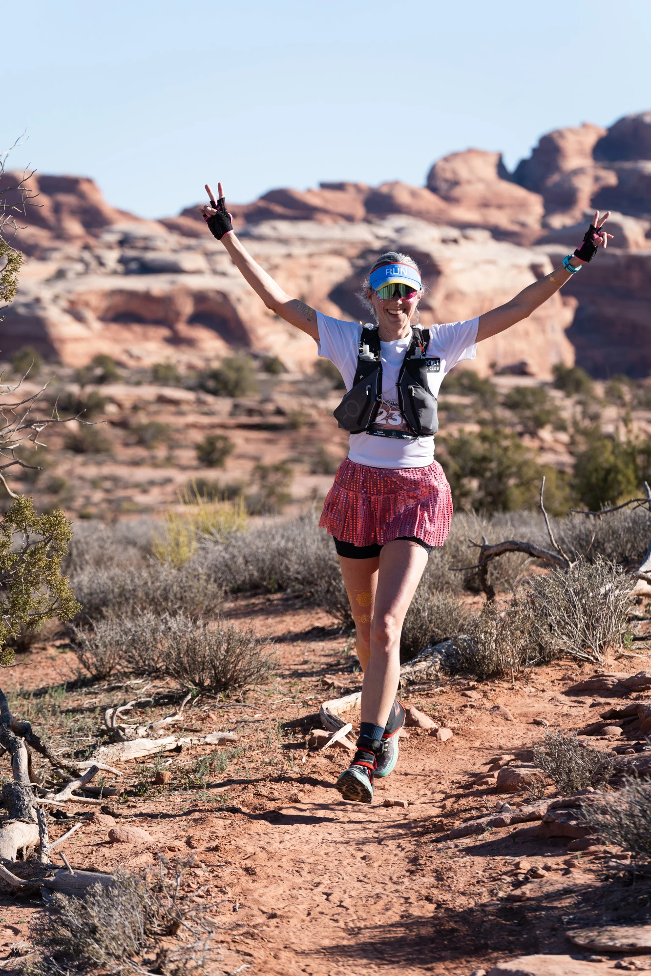 A trail runner raises both arms while moving through a desert course.
