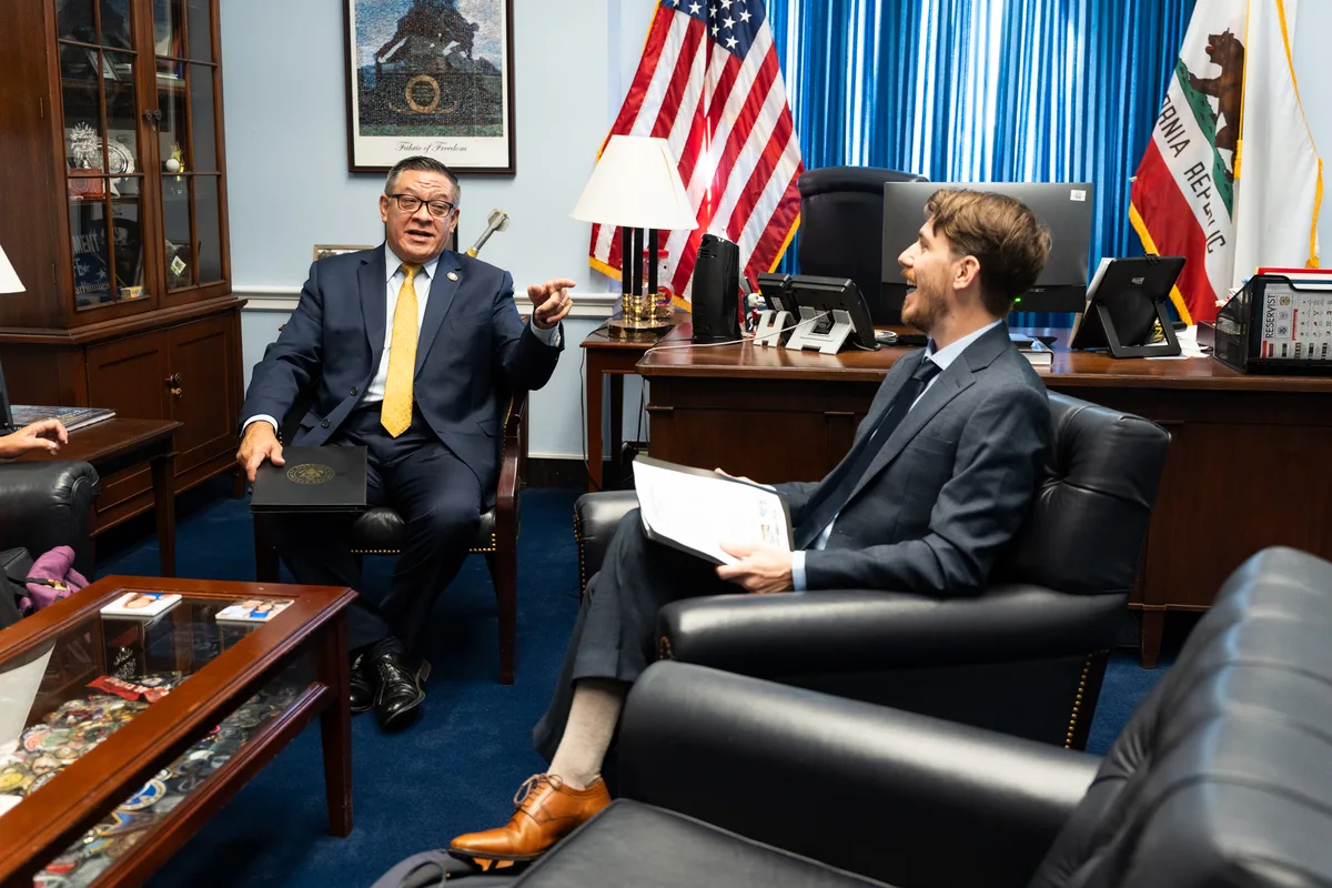 Two advocates speak together in an office with United States flags behind them.