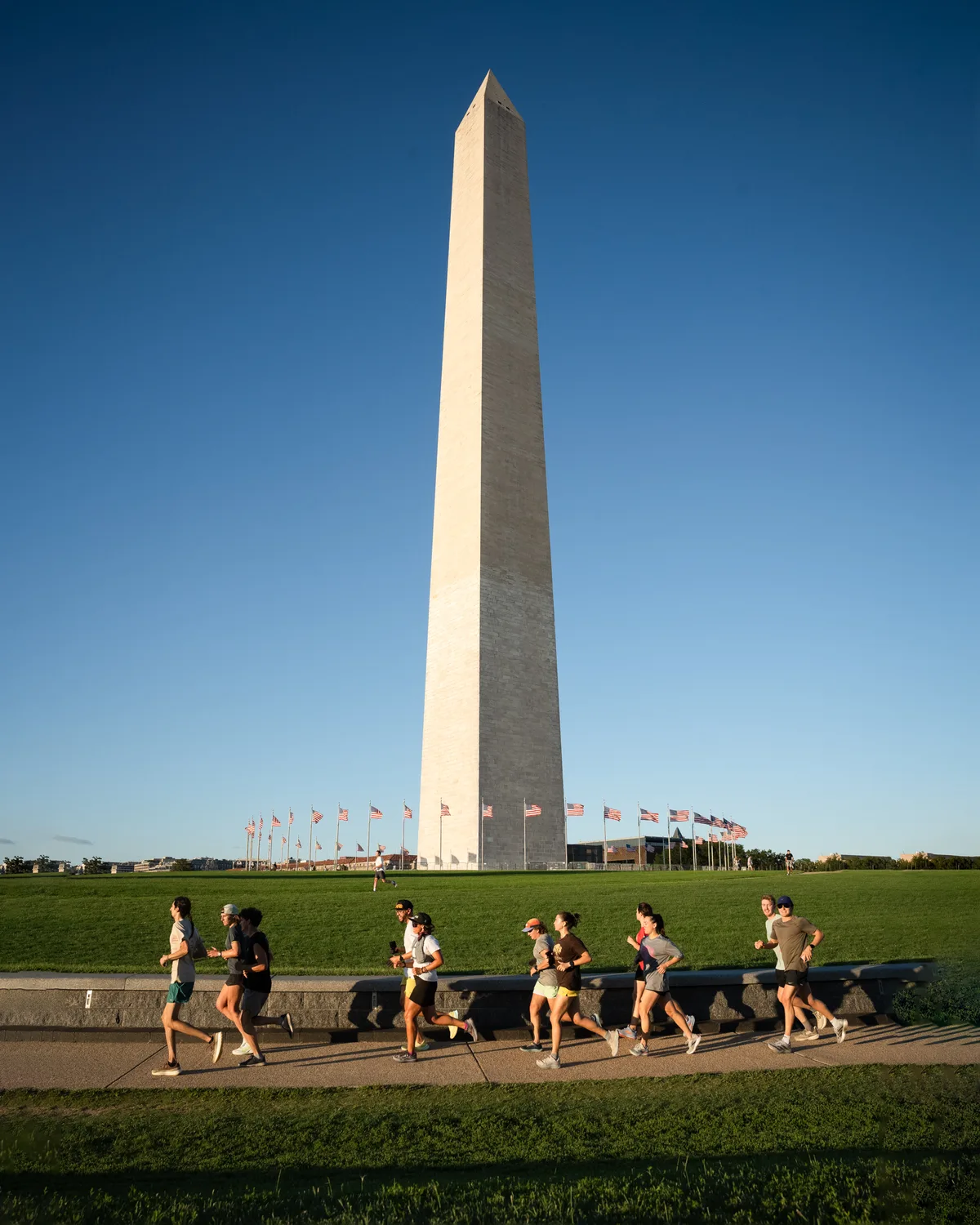 A group runs past the Washington Monument beneath a blue sky.