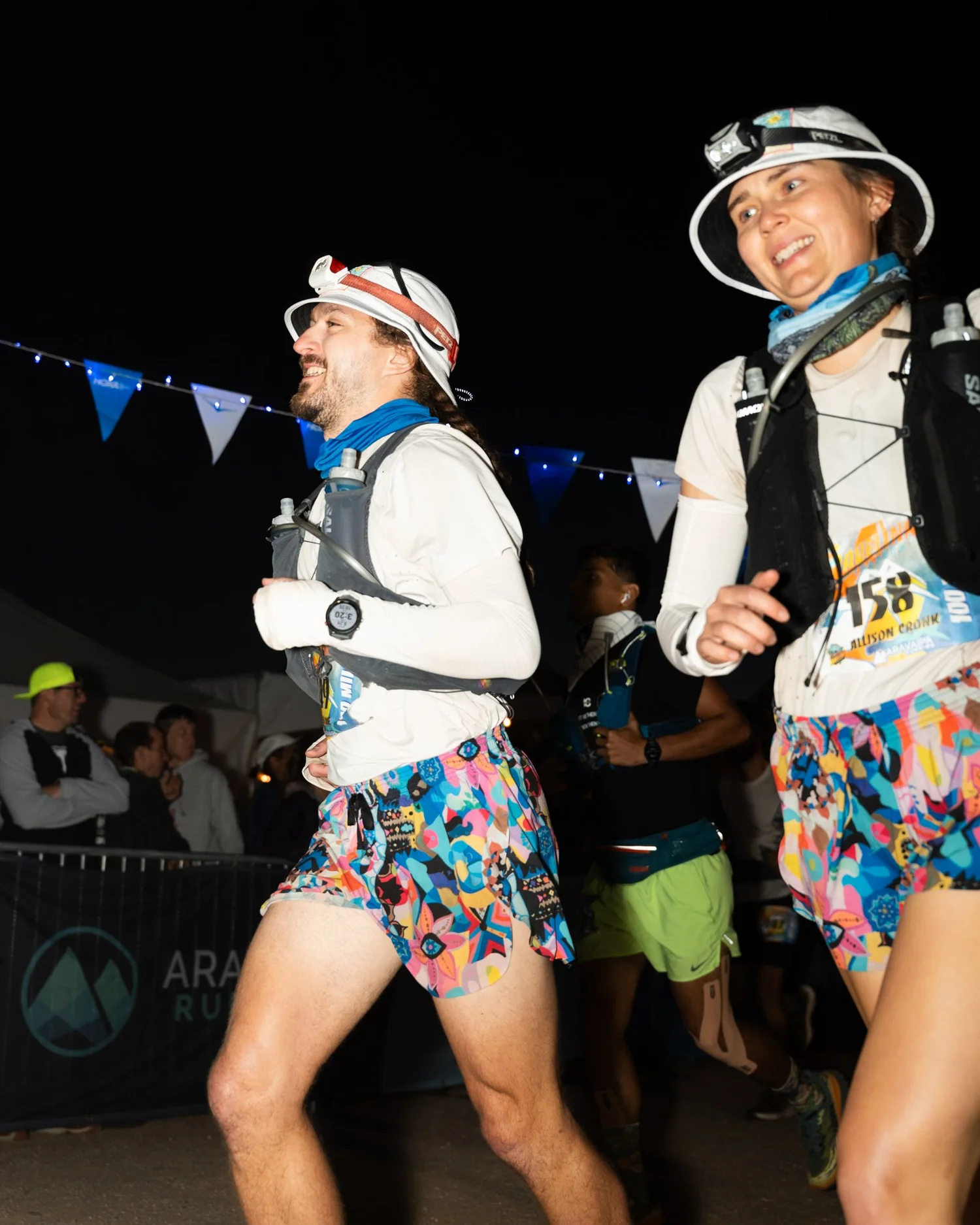 Two Javelina Jundred runners move through the course at night wearing headlamps and colorful shorts.